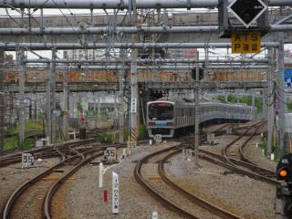 大崎駅ホーム端から地下へ進入していくりんかい線70-000形電車を見る。中央に見える錆びた橋桁は百反歩道橋。その奥では横須賀線・東海道新幹線が直交している。